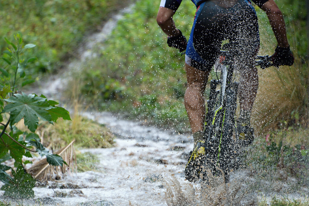 A mountain bike rider cycles into a large puddle creating lots of spray.